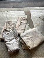 Four different sized beige canvas painting tarps folded and stacked on a diamond plate metal surface.