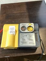 Top view of Air Man 12 VDC air compressor pump showing yellow and gray casing, pressure gauge, control knob, and user instructions.