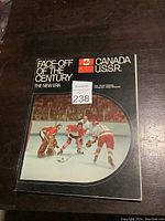 Front cover of the souvenir book featuring hockey players and flags of Canada and USSR with the title 'Face-Off of the Century'.