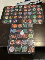 Photo showing multiple sheets of Disney Pocahontas pogs laid out on a dark wooden table, displaying colorful images of characters and scenes from the movie.