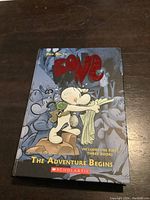 Front cover of the hardcover book titled Bone The Adventure Begins featuring main character and Scholastic branding.