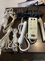 Photo of six various power bars and surge protectors on a wooden table, showing cords and outlet configurations.