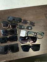 Photo showing ten pairs of women's sunglasses arranged on a wooden surface with auction lot number 149 visible