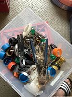 Clear plastic bin holding assorted plumbing items such as clamps, valve handles, and a pipe cutter with blue handles.