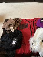 Various women's clothing items laid out, mainly showing a red dress with black lettering and other garments with tags attached.