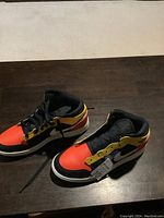 Pair of Nike Air Jordan Air Force high top sneakers displayed on a wooden surface. One shoe has laces, the other is missing a lace.