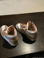 Pair of Nike Air Jordan Air Force 1 high top sneakers in white and tan placed on dark surface.