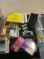 Full view of boxes and bins containing various office supplies including pens, pencils, calculator, and accessories