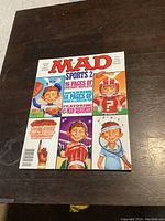 Photo of one Mad Magazine from 1990 showing a colorful cover with a sports theme, multiple caricatured figures and large red Mad title.