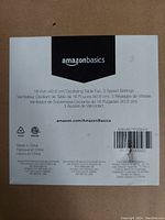 Close-up of the product label on packaging specifying Amazon Basics branding, 16-inch oscillating table fan, three speed settings, measurements in inches and centimeters, product barcode, and manufacturing details.
