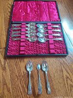 Full view of the 12-piece antique silver plated spoon and tong set displayed in red fabric-lined case with all pieces arranged inside and 3 pieces displayed outside.