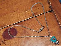 Full view of the silver chain necklace with trapezoidal turquoise and coral pendant lying on wooden surface.