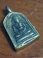 Close-up of the antique bronze pendant featuring a reclining Buddha with Sanskrit text, showing worn texture and detailing.