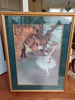 Framed print showing ballerina on stage with male figure behind curtain, filmed with reflections in window, complete frame visible.