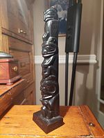 Slender black carved Tahnoo Pole replica with detailed Haida figures, standing upright on a wooden surface.