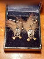 Pair of indigenous tribal earrings displayed inside a black jewelry box. Each earring features a silver face with gold nuggets and brown fur  attached, with silver hook ear wires.
