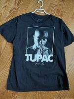 Front view of black XL T-shirt showing Tupac Shakur photographic print with hands clasped in prayer, TUPAC text and signature below it