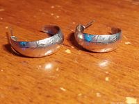 Pair of small hoop earrings made of sterling silver with engraved detailed pattern, shown on wooden surface.