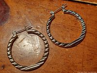 Pair of sterling silver hoop earrings with textured criss-cross design laid flat on a wooden surface