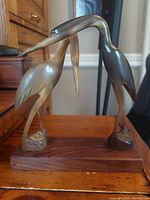 Front angle showing both cranes touching beaks with wooden base visible.