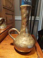 Antique brass cast pouring vessel front angle showing bulbous base and curved finger hold handle on side.