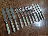 Photo showing 12 piece cutlery set laid out on wooden floor, including six knives and six forks with ivory-colored handles and EPNS stamped metal.