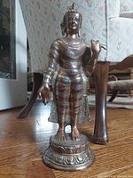 Front view of the standing Buddha metal statue showing detailed robe bands, cape, lotus pedestal, and hand gestures.