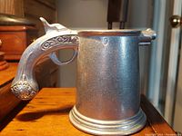 Side view of pewter tankard featuring musket-shaped handle with ornate details