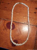 Full view of vintage natural luster pearl necklace laid on a wooden surface showing uniform pearl shapes and clasp at the end.