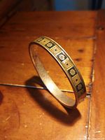 Metal bracelet on wooden surface visible at an angle showing floral and square gold motifs on black background band