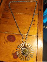 Full view of the necklace laid out showing the metal chain and the sunburst medallion with an agate inset stone.