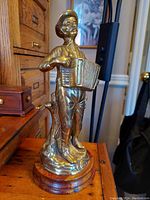Front and side views of the vintage brass figurine of a man playing an accordion, mounted on a wooden base.