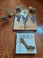 Overview of three miniature shoes individually encased, placed above two calendars on a wooden floor