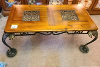Full view of the wooden coffee table showing the top with two square metal filigree inlays and the legs shaped as elephant heads and trunks ending in round bases.