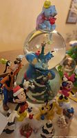 Disney Christmas snowglobe featuring Genie and Tinker Bell inside the globe, Dumbo on top, and surrounding Disney character figurines.