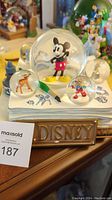 Overall view showing the set of multiple snow globes including large Mickey in center and smaller globes with other characters arranged on a surface with a paintbrush and Disney sketches motif.