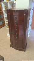 Front view of the dark cherry wood jewelry cabinet showing 8 drawers with metal handles and a keyhole.