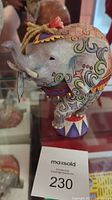 Close-up of side view of Jim Shore carved elephant figurine, showing decorative colorful painted patterns on body and head with red flower on top and jingle bells.