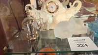 Shelf display showing the three items including the clear glass elephant perfume bottle, cream colored elephant clock, and frosted glass elephant figurine.