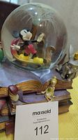 View of Mickey Mouse inside snow globe with fireworks and book base showing Ariel and Cheshire Cat figurines.