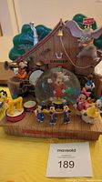 Front view of the snow globe with Mickey Mouse inside and surrounding Disney character figurines on a wooden base with backdrop.