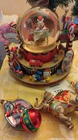 Full view of Mickey Mouse Christmas snowglobe with elves climbing around base and 3 blown glass elephant ornaments in front