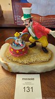 Front view of the Ron Lee Dumbo sculpture featuring Dumbo on a red circus drum and the ringmaster wearing bright colorful attire on a natural marble base.