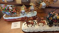 Photo showing gold sleigh with children and gifts, eight reindeer mounted on snowy base, next to brown stagecoach with four horses on snowy base.