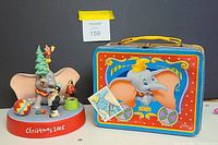 Photo showing Dumbo Christmas 2006 ceramic figurine next to vintage metal Dumbo lunchbox, highlighting condition and details