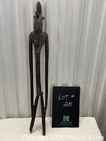 Front view of the tall slender wooden statue of a man with a headdress, legs separated.