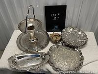 Photo showing all silverplate trays and decorative item arranged on table including two-tier tray, three silver trays of various shapes, and small decorative bowl.