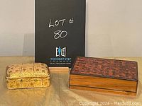 Two decorative boxes side-by-side on a gold-colored cloth with a black sign in the background labeled 'Lot #80'.