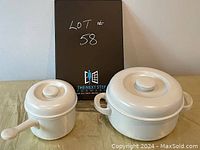 Two white cooking pots displayed side by side, smaller pot with long handle and lid, larger pot with two handles and lid.