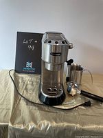 Front view of DeLonghi machine with attached portafilter, pitcher and filter basket on table